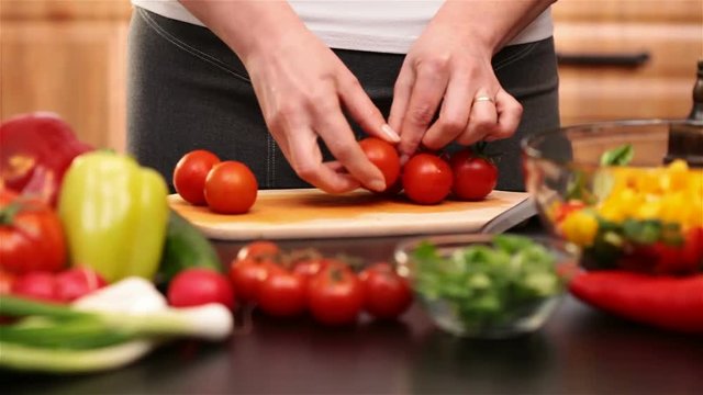 Woman hands preparing cherry tomatos for a vegetables salad plucking them off the stem - side view  of the cutting board at the kitchen table, camera zooming in