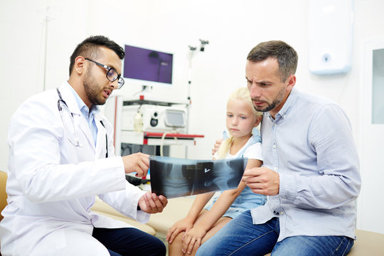 Doctor showing x-ray images of little girl to her father in hospital office