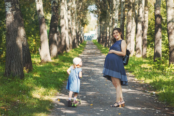 happy pregnant mother is walking with her little daughter in the park, happy family photo