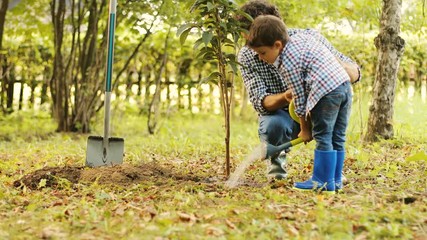 Portrait of a boy and his dad watering a tree. Dad helps his son. Blurred background