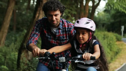 Closeup. Portrait of a little girl and her father. Dad teaching his daughter to ride a bike. Lets her go. Moving camera. Blurred background
