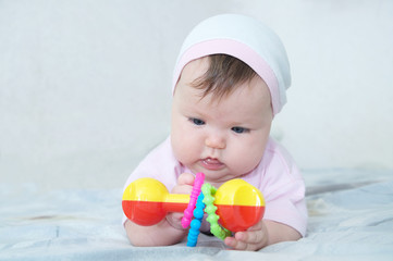 Early brain development. concentrated little baby girl  playing with rattle lying on bed
