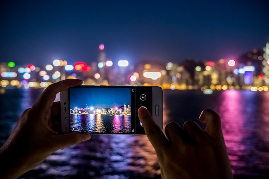 Woman using her Mobile Phone to take photo of city view, night light Background