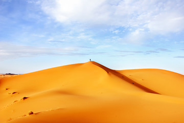 High sand dunes of the Sahara desert against a blue sky with clouds.
