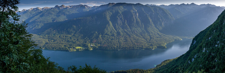 Obraz premium Panorama view of the blue lake Bohinjsko jezero surrounded with green grass and trees. Summer in Julian Alps, Bohinj, Slovenia, Europe.