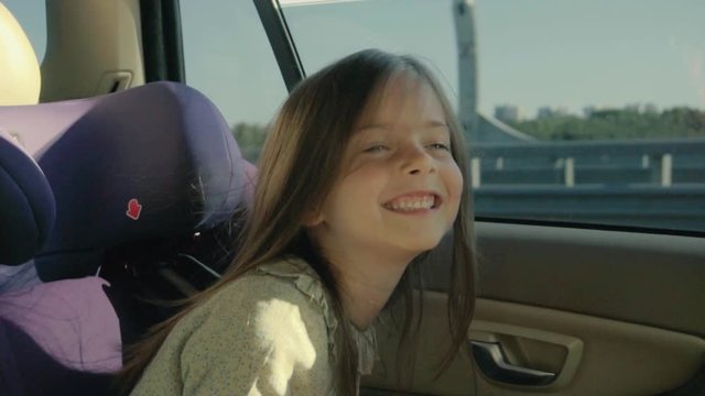 Cute little girl riding in the car at back seat and looking throught the window.