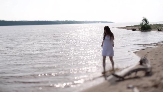 A girl in a white dress runs along the shore along the water.