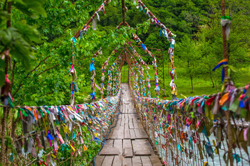 A pedestrian suspension bridge across the river in Abkhazia. Multicolored ribbons are hung on it....
