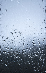 Rain drop on window glass with abstract cold blurred bokeh background.