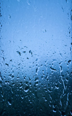 Rain drop on window glass with abstract ice cold blue blurred bokeh background.
