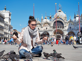 Beautiful young woman feeding pigeons on the Piazza San Marco