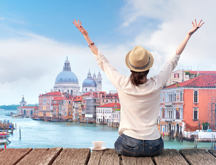 Woman traveler in hat with arms raised and cup of coffee on bridge in Venice