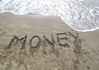 Fototapeta premium word MONEY written on the sand and the wave that is erasing the