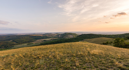 Sunset landscape panorama, hills in golden hour, small village in valley, beautiful colors and clouds.