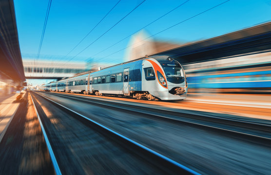 Fototapeta High speed train in motion at the railway station at sunset in Europe. Modern intercity train on the railway platform with motion blur effect. Industrial scene with moving passenger train on railroad