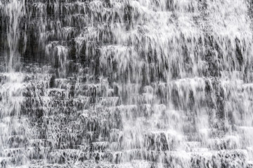 Closeup of refreshing waterfall flowing over tiered rocky land in miniature cascades