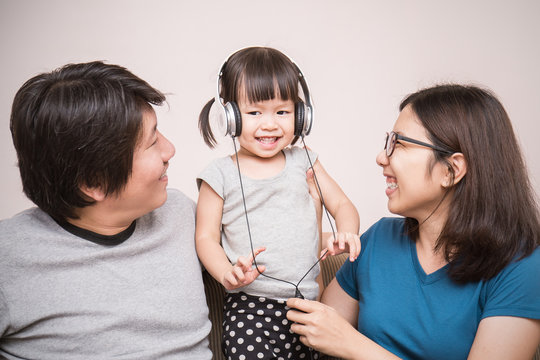 Closeup Happy Asian Parents And Baby Girl In Sofa Using Tablet And Headphones, Asian Parents With Toddler Daughter Girl Listen To Music In Their Living Room.