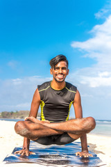 Asian yoga man practice yoga on the beach with a clear blue sky background. Yogi on the tropical beach of Bali island, Indonesia.