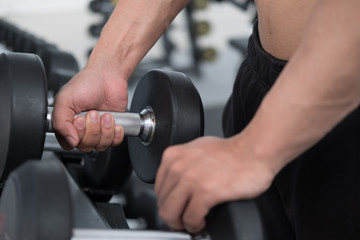 Naklejka na ściany i meble young man execute exercise in fitness center. male athlete choose dumbbell in gym. sporty guy working out in health club.