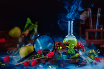 Nutritionist workplace with laboratory tubes, green smoothie, magnifying glass and assorted berries, raspberry and blackberry with mint leaves. Dark food photography, science concept.