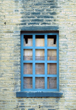 boarded up blue window in a derelict house with dirty brick wall