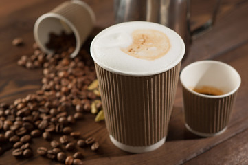 Latte and espresso in paper cups on a wooden background with scattered coffee beans