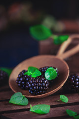 Tiny wooden bowl with fresh blackberries and mint leaves. Dark food photography with copy space.