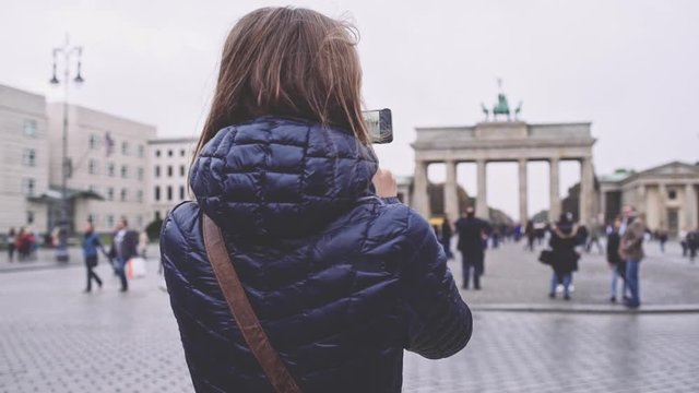 Woman Taking Pictures of Brandenburg Gate in Berlin with SmartPhone. SLOW MOTION. Young woman tourist with cellphone photographing Brandenburger Tor. Travel in Germany.