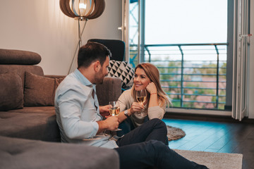 Romantic couple drinking wine at home while sitting on floor.
