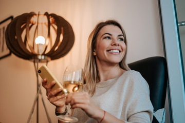 Woman having a glass of wine while using her phone.