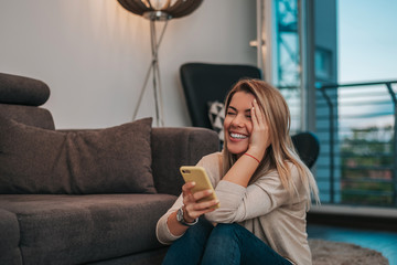 Portrait of a smiling young woman sitting on floor at home with cell phone.