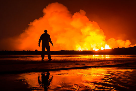 Man standing on beach with volcanic eruption in background