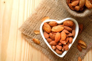 Almond nuts in the shell In a heart shaped bowl on sackcloth and wooden floor.