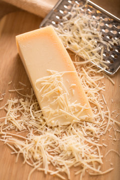Parmesan Cheese and Grater Above. an above view of a block wedge of parmesan cheese with shredded pieces all around and a metal cheese grater on a cutting board