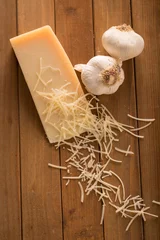 Fototapeten Shredded Parmesan and Wedge with Garlic Above. an above shot looking down on a wedge of parmesan cheese and two cloves of garlic with shredded slices of cheese on top © revelpix