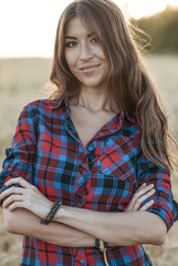 Fototapeta premium Beautiful girl field. Summer in nature. Happy smiling looking in frame. In the evening shirt a brunette woman, a close-up portrait, a concept of fun. Close-up portrait.
