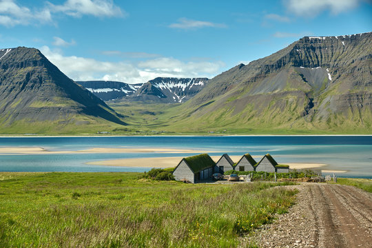 Travel to Iceland. beautiful sunrise over the ocean and fjord in Iceland. Icelandic landscape with mountains, blue sky and green grass on the foreground. View of the road to houses in the north-west