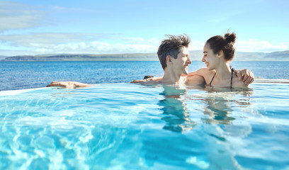Young cheerful girl with man swimming in water of pool looking each other on background of sea, Iceland, West Fjords.