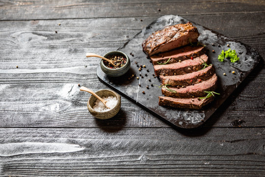 Sliced grilled roast beef with salt and pepper on marble plate on wooden old rustic table Black background. 