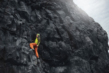 male rock climber. rock climber climbs on a black rocky wall on the ocean bank in Iceland, Kirkjufjara beach. man makes hard move without rope.