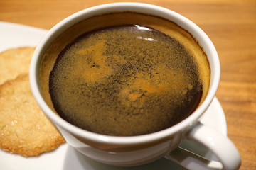 Closed up a cup of black coffee in a white cup with blurred cookies in background 