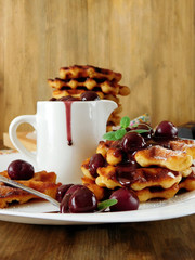Waffles with cherry and chocolate sauce served on a white plate and in the white gravy boat