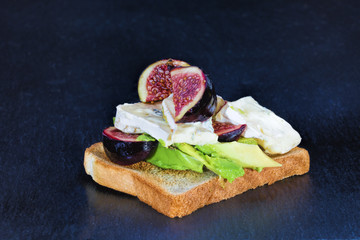 Frische Avocado, Feigen und Blauschimmelkaese auf Toastbrot als Vorspeise auf schwarzem Grund