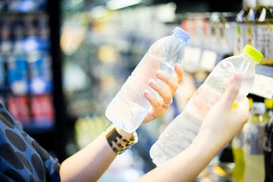 woman choosing cold bottle of water or beverage on shelves in supermarket store.