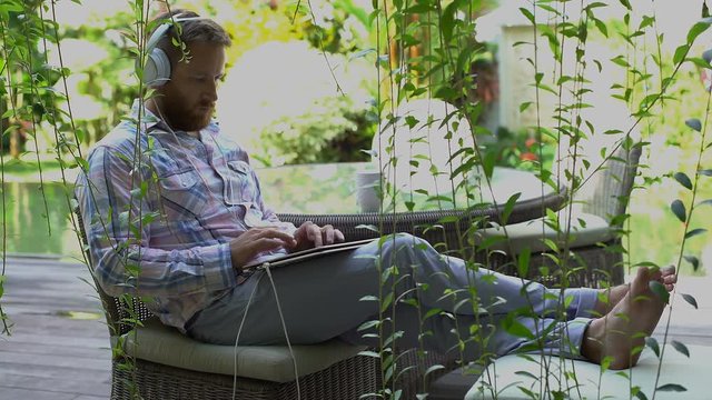 Man listening music in the garden and using modern notebook
