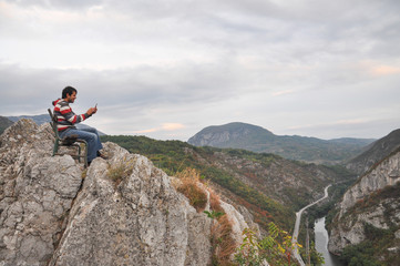 Man with phone on cliff taking photo. Man sitting on edge of the cliff and work on mobile