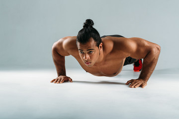 Muscular man doing push up exercises in studio, front view