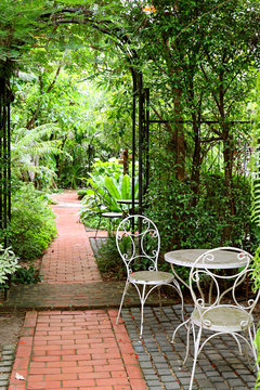 Vertical photo of white wrought iron table and chairs in the garden with bricks paved walkway 
