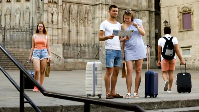 Couple of young tourists with baggage walking with map at street
