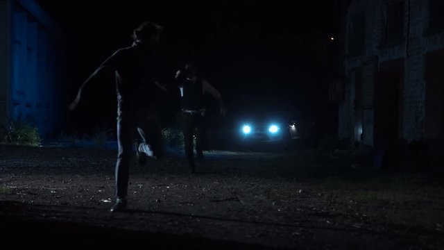 Brave police officer running after a dangerous suspect or wanted delinquent on a dark street in the suburbs at night